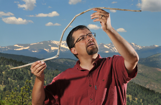 Figure 3: Dr. Craig M. Lee examining the 10,300 year-old dart he found near Yellowstone National Park. The Colorado Front Range is in the background.